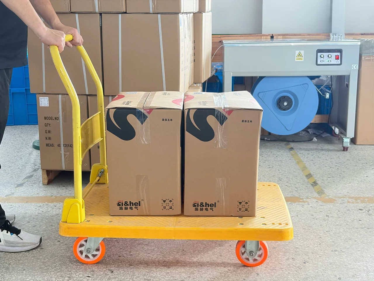 Packaged Shieldhz cartons on a hand trolley near a packing station